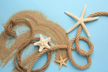 Fototapeta na wymiar Beautiful sea stars, rope and sand on light blue background, flat lay