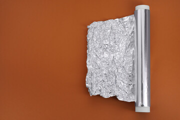 One roll of aluminum foil on brown background, top view. Space for text