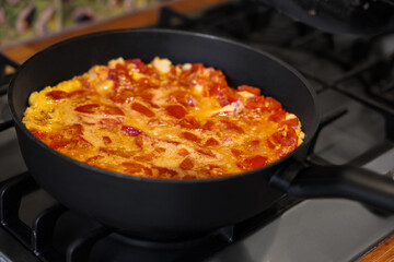 Tasty fried eggs with tomatoes in frying pan on stove, closeup