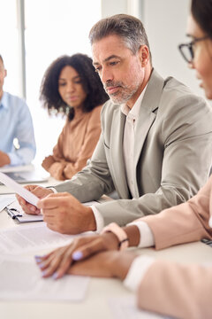 Busy Senior Indian Businessman Investor Bank Client Reading Document At Office Team Meeting With Executive Professional Financial Law Experts Group. Consultancy And Advisory Services, Vertical Shot.