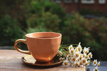 Cup of delicious chamomile tea and fresh flowers outdoors
