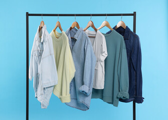Rack with stylish clothes on wooden hangers against light blue background