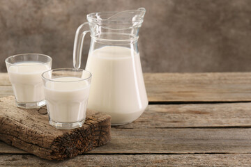 Jug and glasses of fresh milk on wooden table, space for text