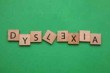 Word Dyslexia with inverted letter E of wooden tiles on green background, flat lay