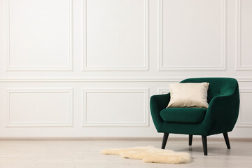 Comfortable armchair with cushion near white wall indoors. Space for text
