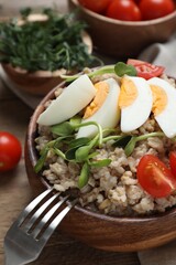 Tasty boiled oatmeal with egg, tomatoes and microgreens served on wooden table, closeup