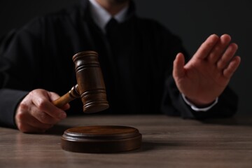 Judge with gavel showing stop gesture at wooden table against black background, closeup