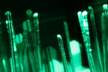 Optical fiber strands transmitting green light on black background, macro view