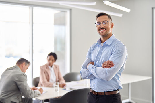Smiling young confident Latin business man manager standing arms crossed at office team meeting. Portrait of happy professional businessman, male company employee leader in board room.