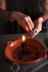 Fototapeta na wymiar woman doing traditional ritual with black candle sea salt pepper in clay plate with herbs and incense and energy management with fire