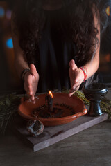 Obraz na płótnie Canvas woman doing traditional ritual with black candle sea salt pepper in clay plate with herbs and incense and energy management with fire