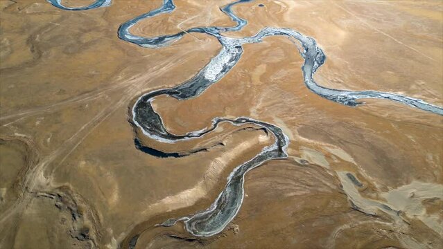 A drone flew over a river in the Mongolian steppes, beautifully capturing the vastness of the grasslands, snow-covered mountains, and flowing rivers.