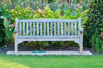 Drewniana ławka ogrodowa w zielonym ogrodzie. Mała architektura grodowa. Park miejsce wypoczynku.