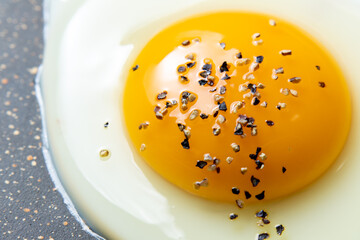 フライパンで目玉焼きを焼く調理シーンのアップ。(粗びきブラックペッパーがけ)
