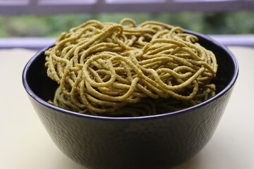 Spinach or palak sev are crunchy fried savory noodles. Indian snack, served in a bowl