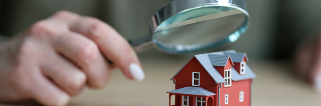 Woman holds magnifier glass above small model of townhouse