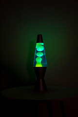 Green lava lamp stands near a white wall in the darkness