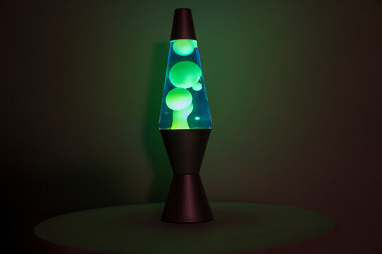 Green and blue lava lamp stands near a white wall in the darkness