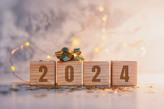 New Year holiday background. Inscription on wooden cubes of the number 2024 with bright glowing lights.