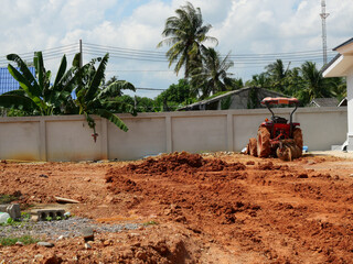 Tractor is plowing and leveling the soil in the construction area with tree with concrete wall and...