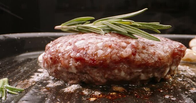 Pork cutlet for burger fried in frying pan. Perfect pork patty is pan-fried with rosemary sprigs, garlic and cherry tomatoes. Cinematic video for burger advertisement. Delicious and juicy pork cutlets