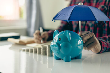 Property insurance guidelines with an umbrella on a piggy bank and a pile of coins on a table - obrazy, fototapety, plakaty