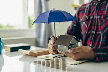 Man holding a blue umbrella and a house Insurance agent holds blue umbrella over modern house model...
