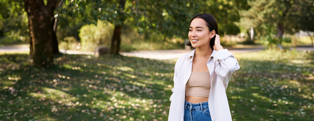Beautiful young asian girl smiling, laughing and walking along park, enjoying summer sunny day