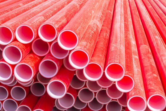 Red polyvinyl chloride pipes for laying electrical cables. Plastic pipe for carrying out communications during construction and repair. Laying pipes in trenches. Background of red long pipes.