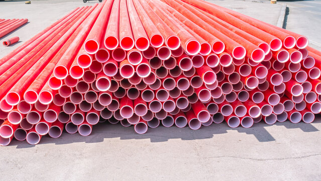 Red polyvinyl chloride pipes for laying electrical cables. Plastic pipe for carrying out communications during construction and repair. Laying pipes in trenches. Background of red long pipes.