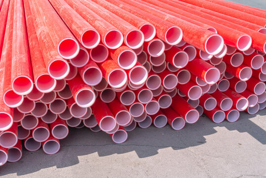 Red polyvinyl chloride pipes for laying electrical cables. Plastic pipe for carrying out communications during construction and repair. Laying pipes in trenches. Background of red long pipes.