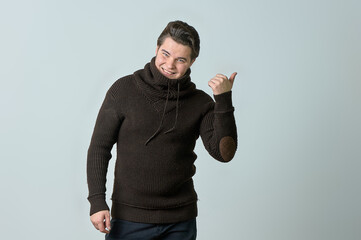 A man on a gray background in a brown sweater showing emotions, shows his hands.