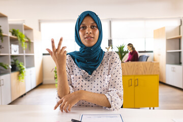 Portrait of happy biracial casual businesswoman with hijab having video call in creative office