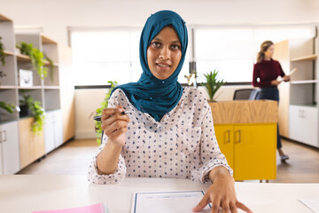 Portrait of happy biracial casual businesswoman with hijab having video call in creative office