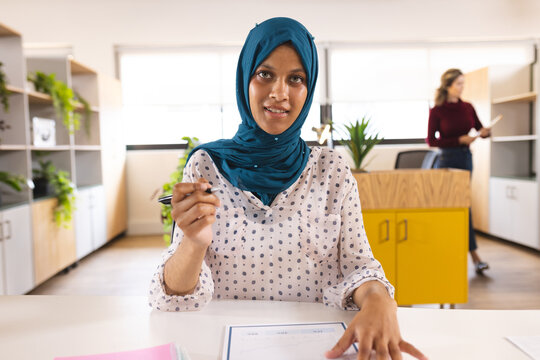 Portrait of happy biracial casual businesswoman with hijab having video call in creative office