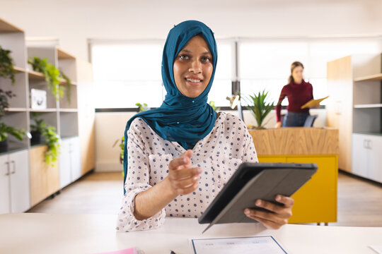 Portrait of happy biracial casual businesswoman with hijab having video call in creative office - Powered by Adobe