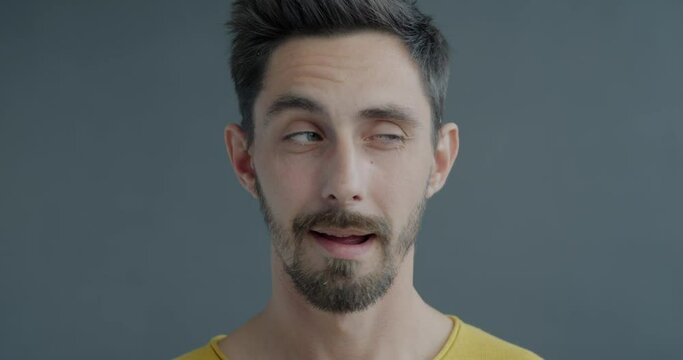 Close-up slow motion portrait of playful guy looking around then winking at camera with charismatic smile. Flirtation and face expression concept.