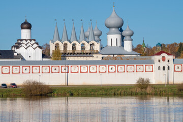 Fototapeta na wymiar View of the belfry of the ancient Tikhvin Assumption Monastery from the side of Tabory lake on a sunny October day. Leningrad region, Russia