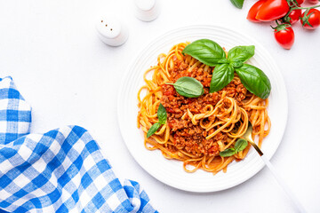 Spaghetti bolognese pasta with minced meat in tomato sauce with green basil leaves on white table background, top view