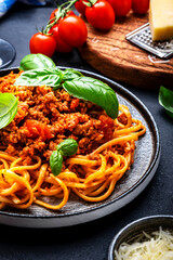 Spaghetti bolognese or pasta with minced meat and tomato sauce with green basil leaves on black table background, top view