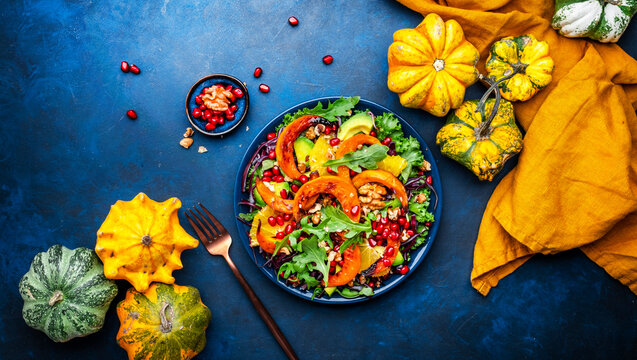 Healthy autumn pumpkin salad with lettuce, arugula, pomegranate seeds and walnuts. Comfort slow food. Blue background. Top view