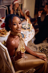 Happy black woman having glass of champagne on Christmas party and looking at camera.