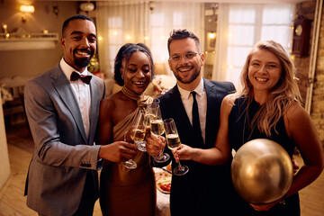 Multiracial group of happy friends toasting while celebrating New Year and looking at camera.