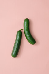 Two dark green cucumbers isolated on pink background. Minimalist scene for cucumber-related product advertisement. Top view, flat lay. Cosmetic advertising.