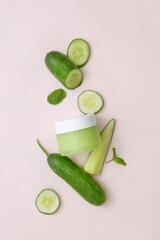 Labelless green lotion jar decorated around with fresh cucumbers on a minimalist background. Cucumbers are rich in vitamins, especially vitamin C, antioxidants that neutralize harmful free radicals.