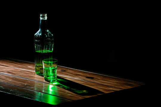 An alcohol kills. An empty alcohol bottle on a table against a dark background. The concept of alcohol dependence. A green empty alcohol bottle on the table 