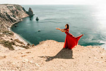 Woman red dress sea. Female dancer posing on a rocky outcrop high above the sea. Girl on the nature on blue sky background. Fashion photo.