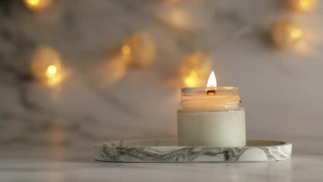 Aromatic burning candle on marble tray with warm lights, cozy home decor, Aromatherapy, autumn atmosphere