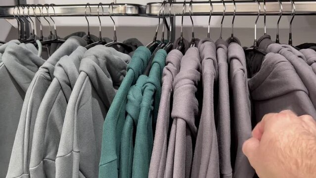 a hanger with different hooded sweatshirts in the store. the hand moves a hoodie.
