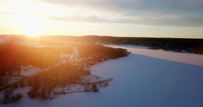 Aerial Ascending Forward Shot Of Back Lit Frozen Portage Lake Amidst Trees Against Sky At Sunset - Houghton, Michigan